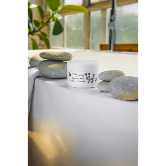 Odylique Baume au Calendula – pot posé sur baignoire entouré de galets zen