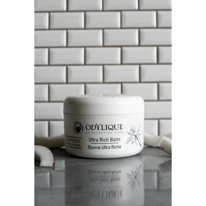 Odylique Baume Ultra Riche – pot fermé sur marbre et carrelage blanc avec noix de coco