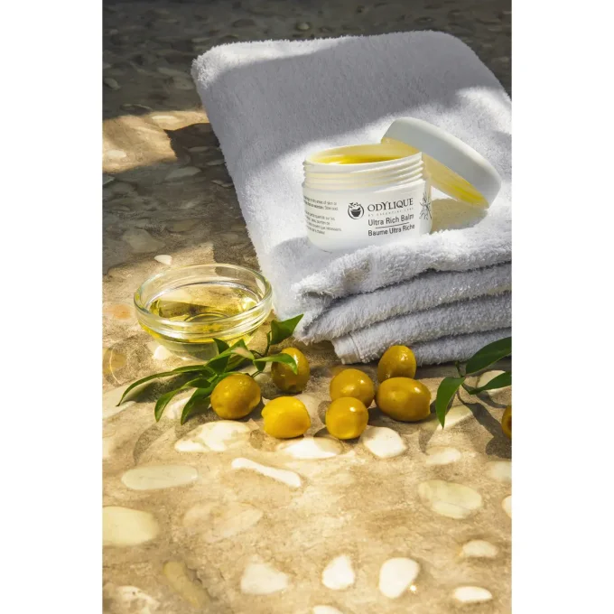 Odylique Baume Ultra Riche – pot ouvert sur serviette avec olives et huile d'olive
