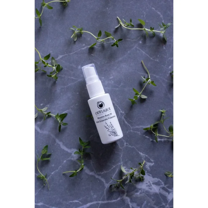Odylique Huile Corporelle Protectrice Anti-Moustiques – flacon entouré d'herbes fraîches sur marbre