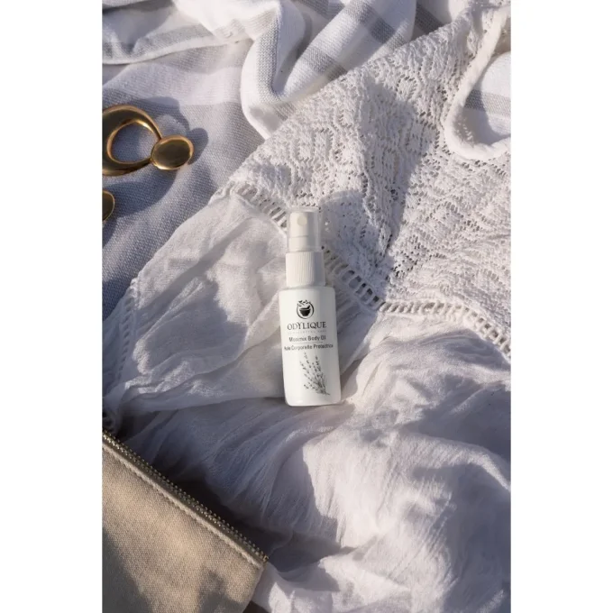 Odylique Huile Corporelle Protectrice Anti-Moustiques – flacon sur tissu blanc estival et bijoux