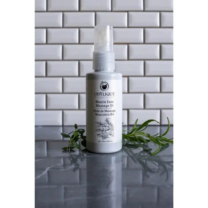 Odylique Huile de Massage Musculaire Bio – flacon sur marbre avec romarin et herbes fraîches