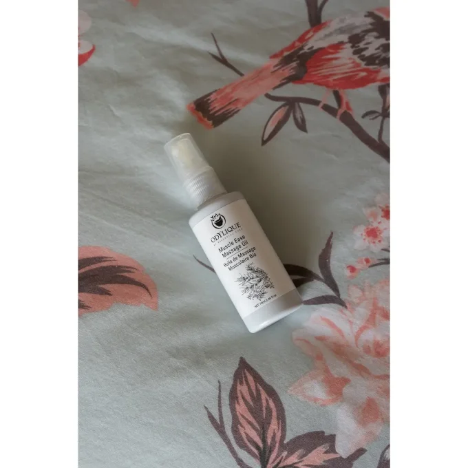Odylique Huile de Massage Musculaire Bio – flacon couché sur tissu fleuri rose et gris
